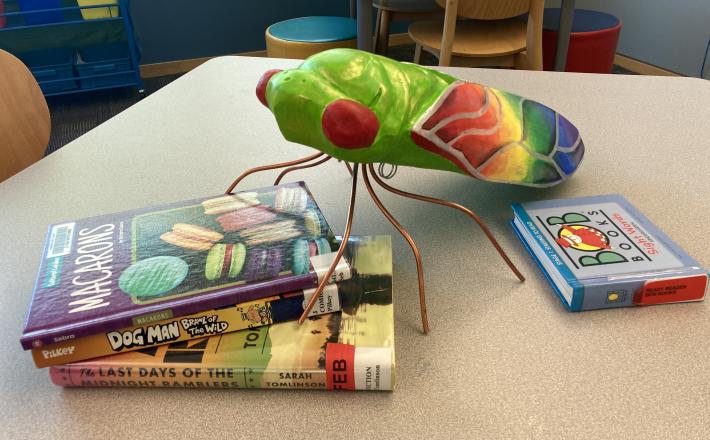 Giant colorful cicada at library on table with books