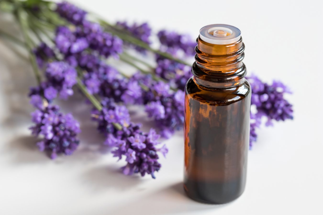 Amber glass essential oil bottle next to a few springs of lavender blossoms