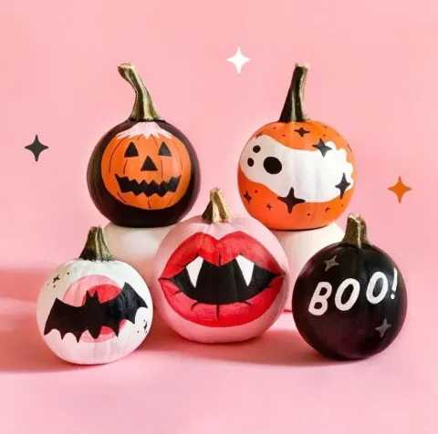 Painted mini pumpkins displaying Halloween images, in front of a pink background